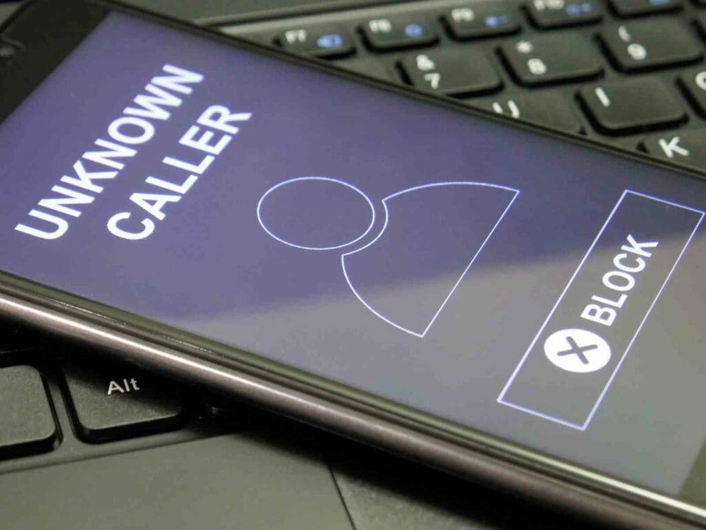 Cellphone laid on a keyboard with the display showing an unknown caller with a button to block caller.