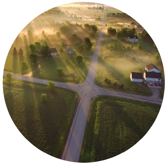 A sky view of fields and landscape with houses and trees, while rising sun's rays are coming from one side.