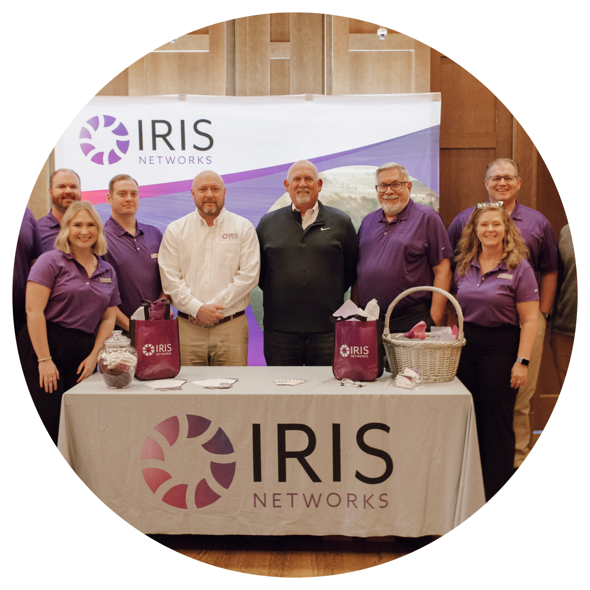 Members of IRIS Networks Team posing for a picture while standing behind the company's table with the IRIS banner at the back