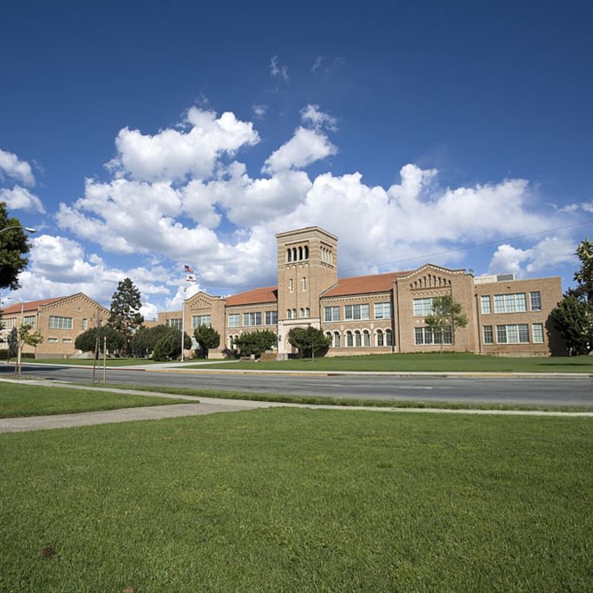 A wide angle composition of a school building facade set under a scattered cloudy and blue sky with a green foreground on a sunny day.